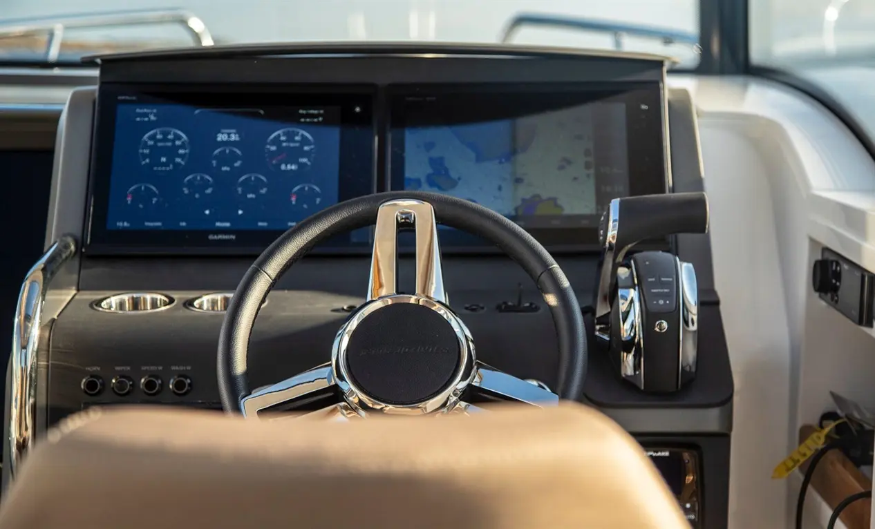Interior view of a modern boat cockpit featuring a steering wheel, dual screens displaying navigational gauges and maps.